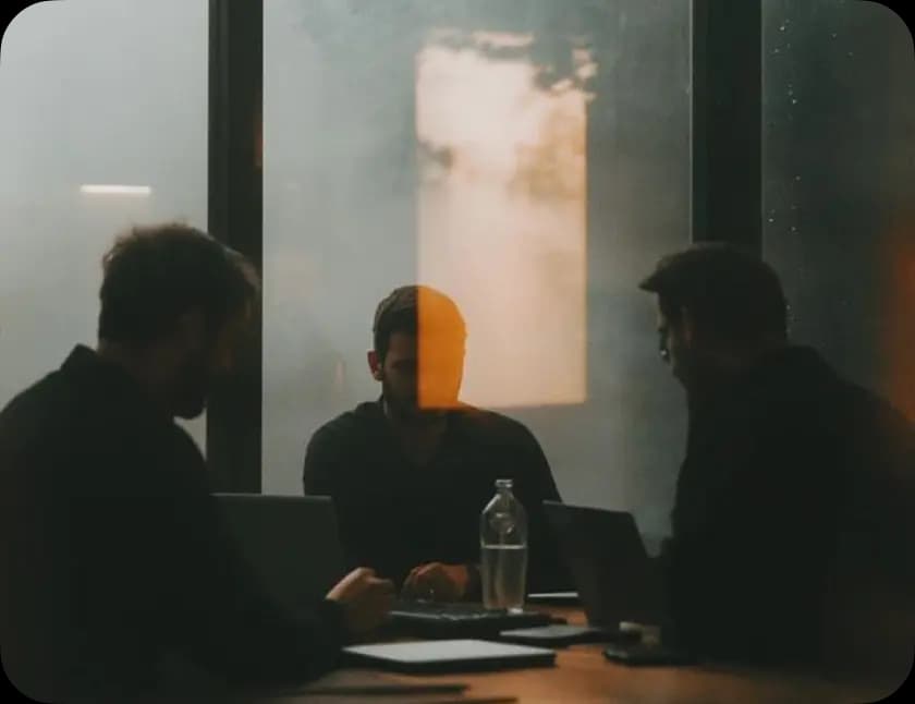 Three colleagues in discussion around a table in a dim meeting room